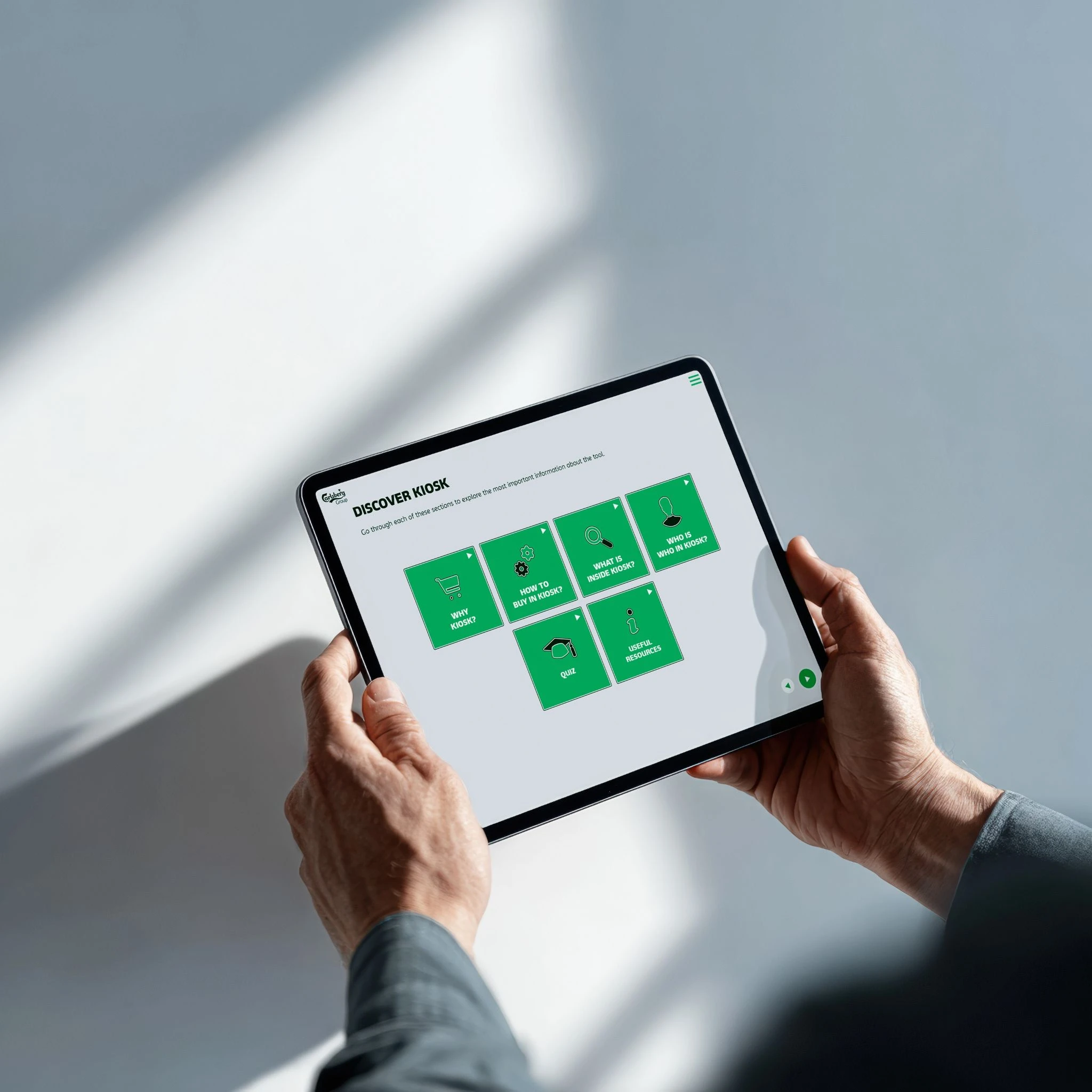 Person holding a tablet displaying the Carlsberg Discover Kiosk learning menu.